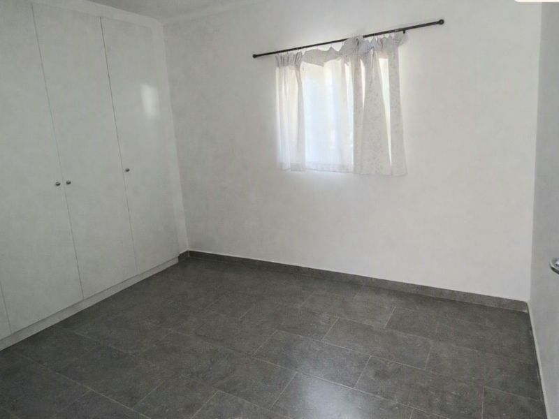 A clean, empty bedroom featuring neutral tiled flooring and built-in cupboards, offering a blank canvas for personalization.