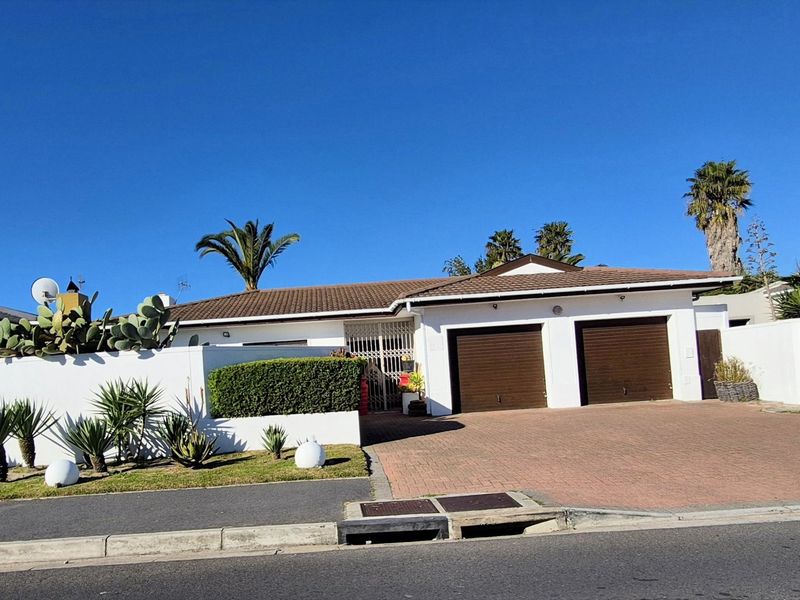 Front elevation of a single-story house featuring a double garage, paved driveway, and a secure boundary wall with landscaped garden elements.