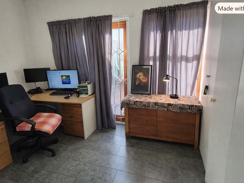 A functional home office space featuring tiled flooring, a built-in cupboard, and direct access to an outdoor area through a security gate.