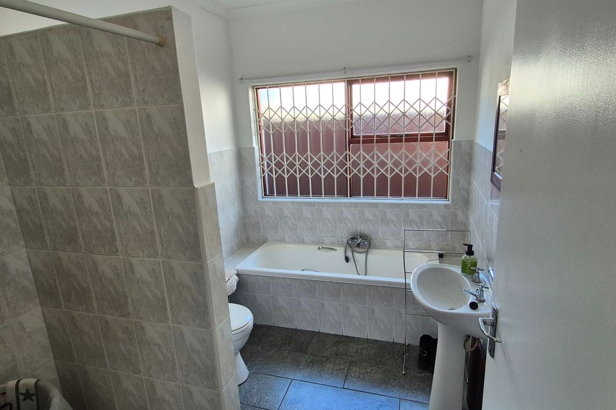 A functional bathroom featuring a tiled shower enclosure, a built-in bathtub, a pedestal washbasin, and a toilet, with security bars installed on the window.