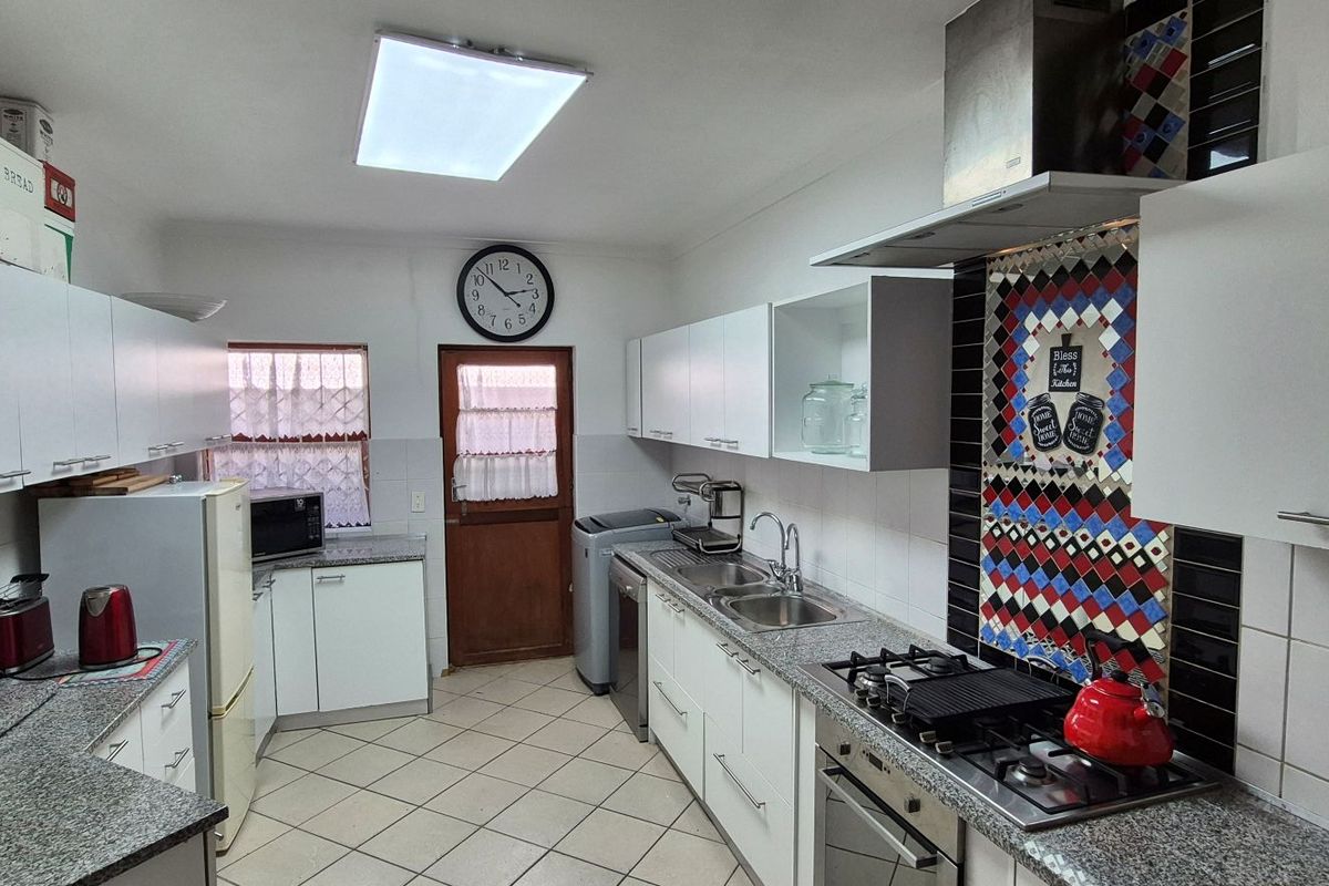Functional kitchen featuring granite countertops, built-in oven, gas hob, extractor fan, and ample cabinetry with tiled flooring.