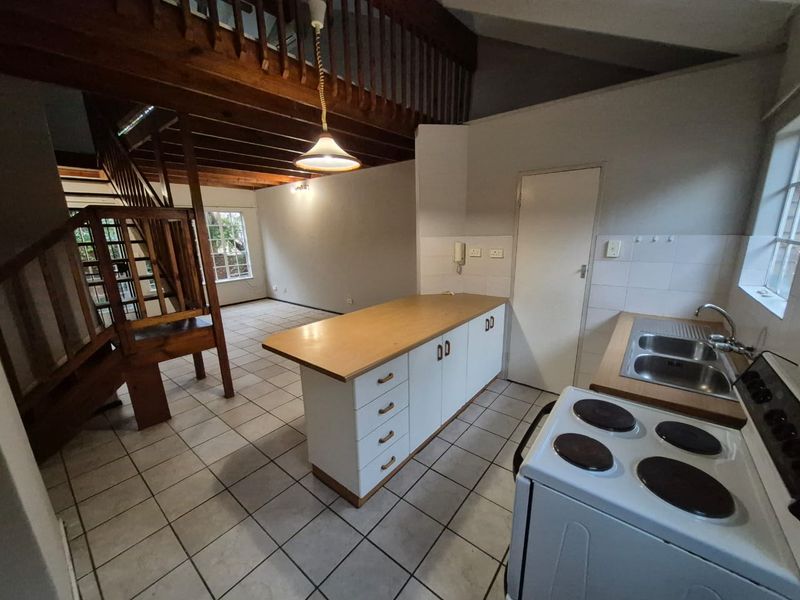 Open-plan kitchen and living area featuring a wooden staircase, mezzanine level, kitchen island, and tiled flooring throughout.