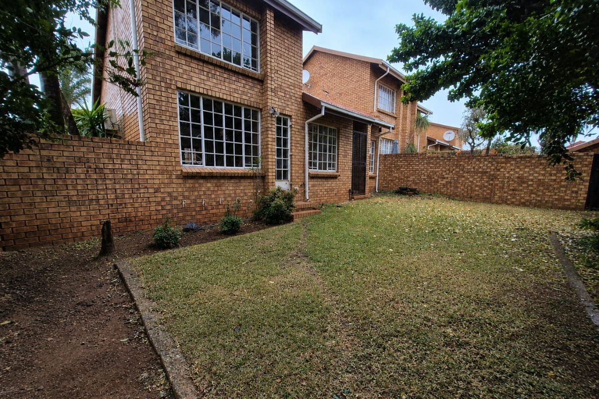 Rear view of a double-story face brick townhouse featuring a private garden with a perimeter wall and grid-pattern windows.