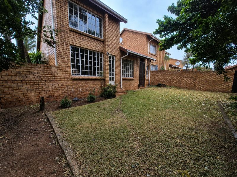 Rear view of a double-story face brick townhouse featuring a private garden with a perimeter wall and grid-pattern windows.