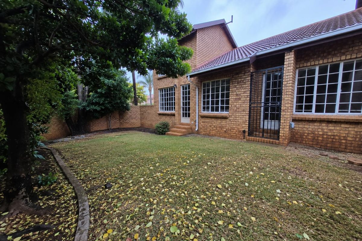 Rear view of a face brick townhouse featuring a private garden, tiled roof, and secure access points with grid-style windows.