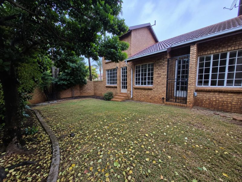 Rear view of a face brick townhouse featuring a private garden, tiled roof, and secure access points with grid-style windows.