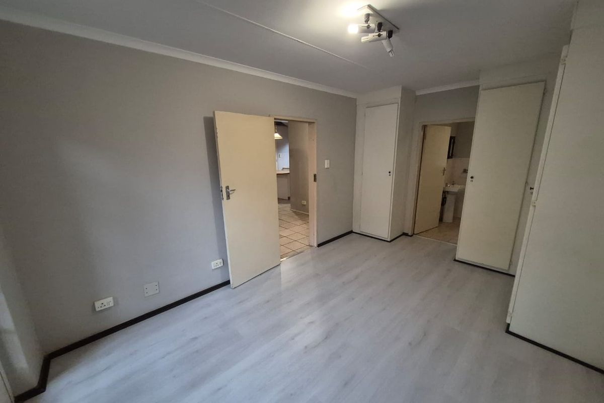 An empty bedroom featuring light-toned laminate flooring, built-in cupboards, and neutral wall finishes, with direct access to an adjacent room and bathroom.