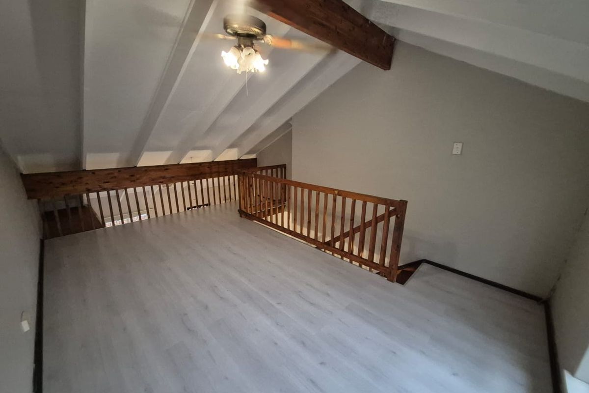 An open-plan loft area featuring exposed timber beams, a wooden balustrade, and modern light-toned laminate flooring.