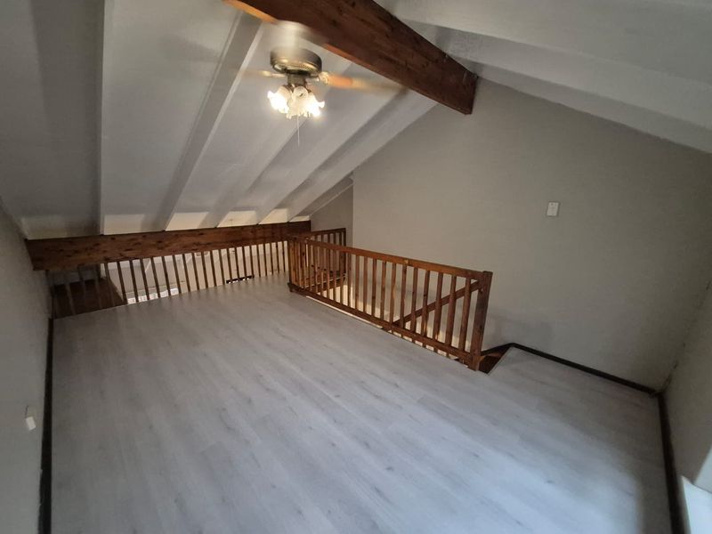 An open-plan loft area featuring exposed timber beams, a wooden balustrade, and modern light-toned laminate flooring.