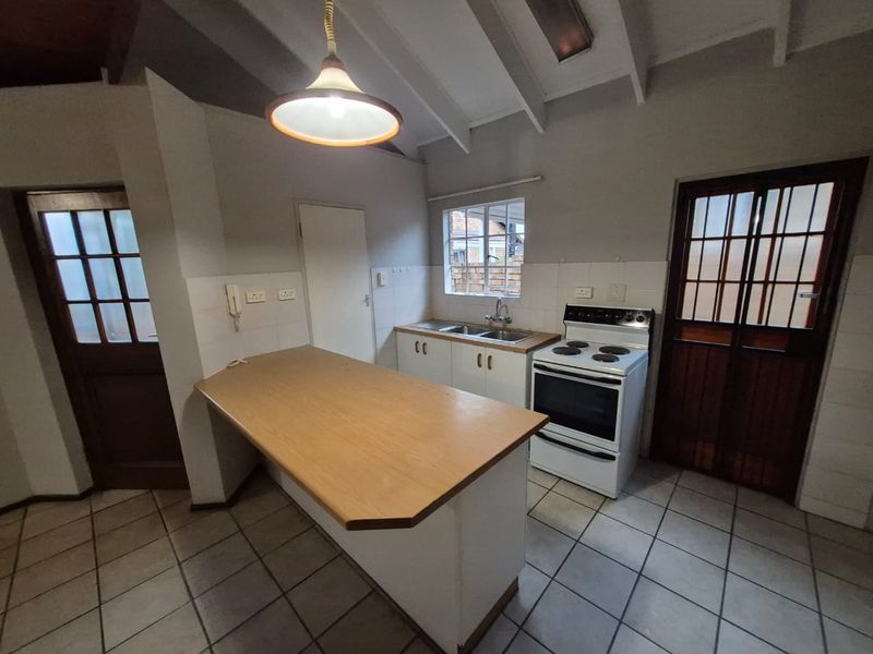 A functional kitchen featuring tiled flooring, built-in cabinetry, a double sink, and a breakfast counter, set under an exposed beam ceiling.
