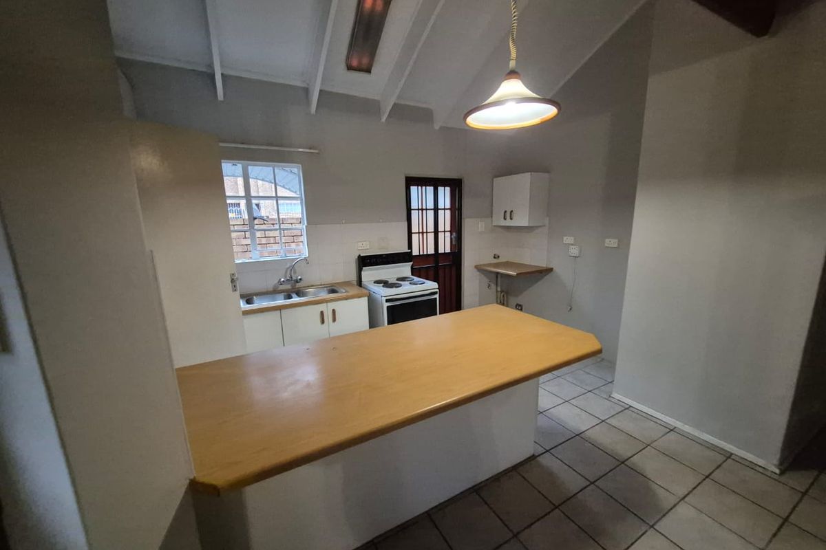 A functional kitchen featuring a breakfast bar, double sink, freestanding stove, and tiled flooring under an exposed beam ceiling.