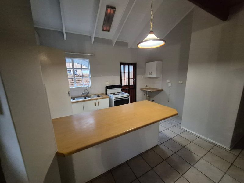 A functional kitchen featuring a breakfast bar, double sink, freestanding stove, and tiled flooring under an exposed beam ceiling.