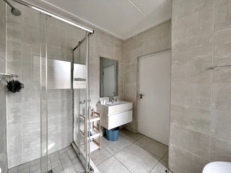 A modern bathroom featuring a glass-enclosed shower, wall-mounted vanity with basin, and neutral floor-to-ceiling tiling.
