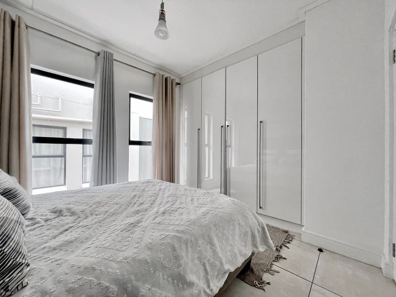 A bright bedroom featuring modern white built-in cupboards, tiled flooring, and large windows allowing for natural light.