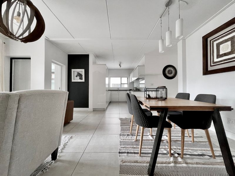 An open-plan living and dining area featuring modern tiled flooring, neutral walls, and a sleek, functional kitchen with built-in cabinetry.