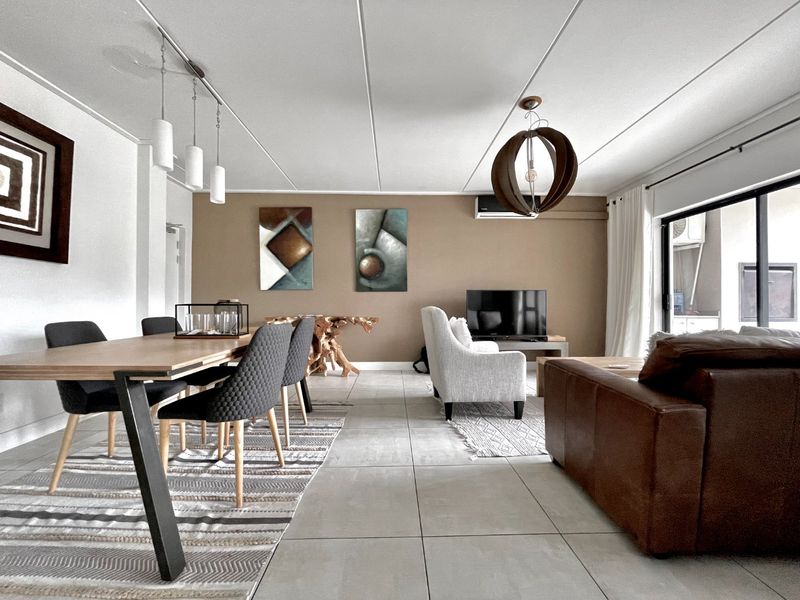 Spacious open-plan living and dining area featuring large format floor tiles, modern lighting, and direct access to an outdoor balcony through sliding glass doors.