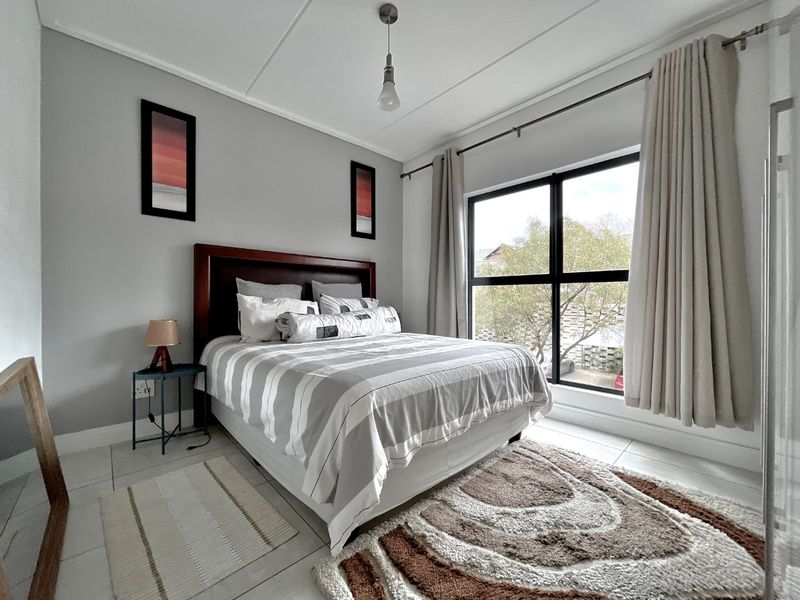 A well-lit bedroom featuring tiled flooring, a large window with curtain rods, and a neutral color palette.