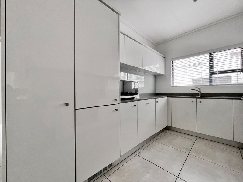 Modern kitchen featuring sleek white cabinetry, dark countertops, tiled flooring, and a functional layout with integrated microwave and stainless steel sink.
