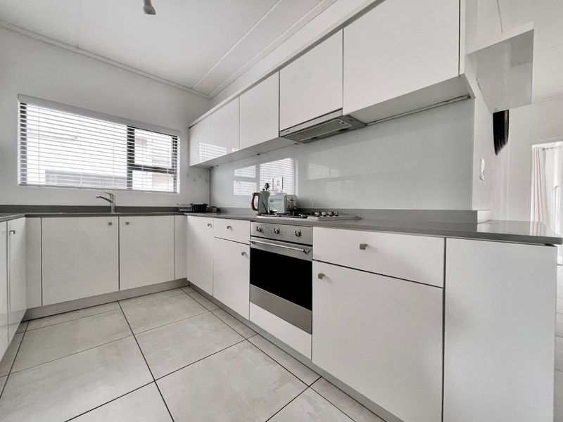 Modern kitchen featuring white high-gloss cabinetry, stainless steel oven, gas hob, extractor fan, and tiled flooring with ample natural light.