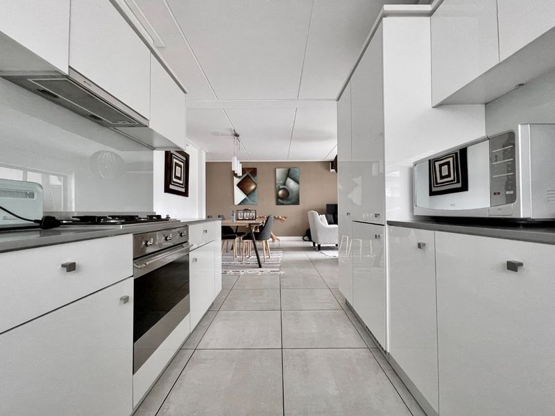 Modern open-plan kitchen featuring sleek white gloss cabinetry, integrated appliances, and large format floor tiles, flowing seamlessly into the dining and living area.