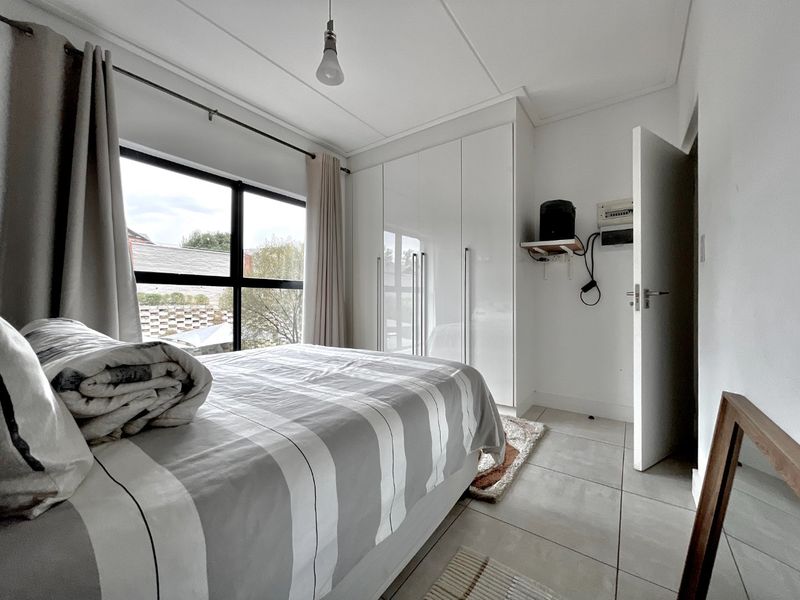 A bright bedroom featuring built-in cupboards, large windows for natural light, and neutral tiled flooring.