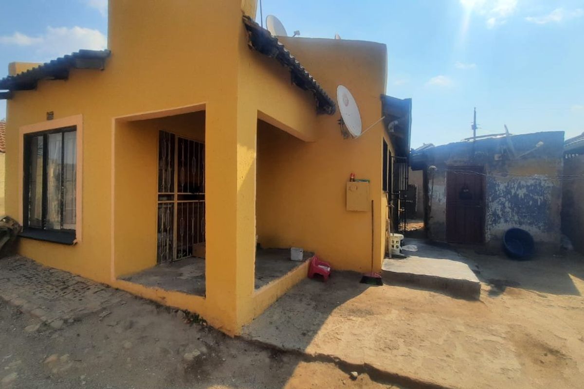 Rear view of the property featuring a covered patio area, concrete paving, and exterior walls requiring maintenance.