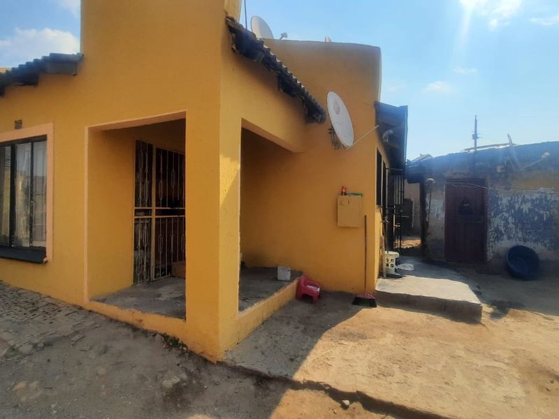 Rear view of the property featuring a covered patio area, concrete paving, and exterior walls requiring maintenance.