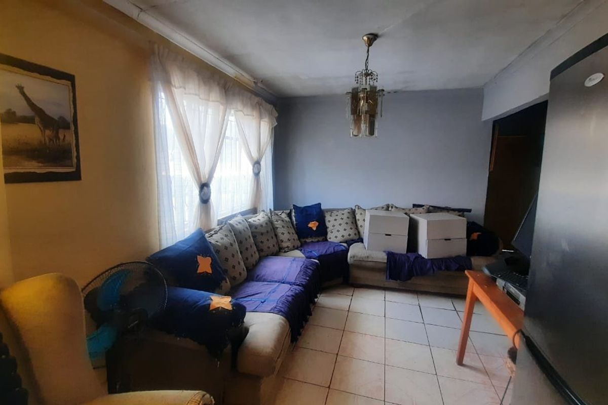 A living room area featuring tiled flooring and a central ceiling light fixture, currently showing signs of wear and requiring cosmetic updates.