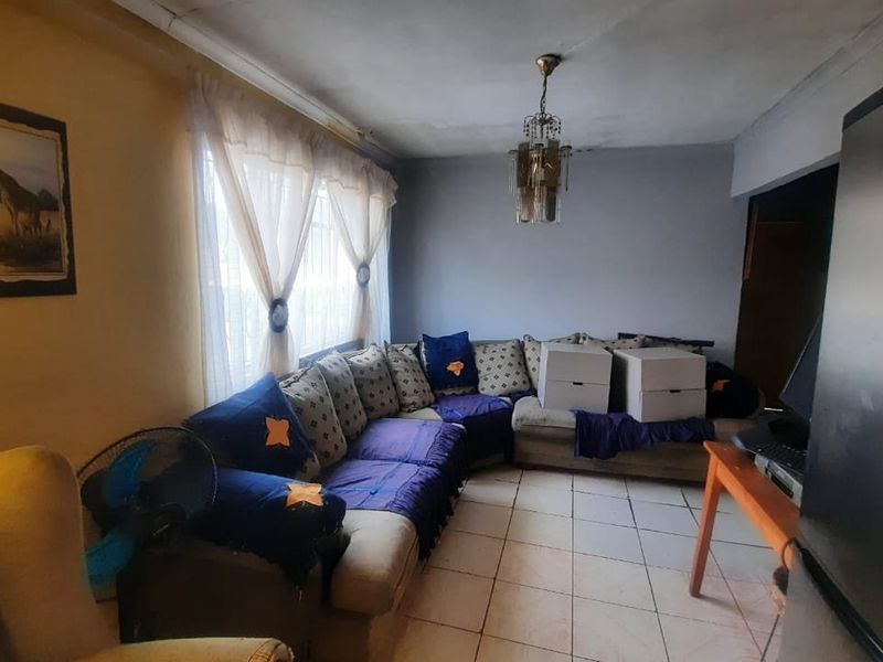 A living room area featuring tiled flooring and a central ceiling light fixture, currently showing signs of wear and requiring cosmetic updates.