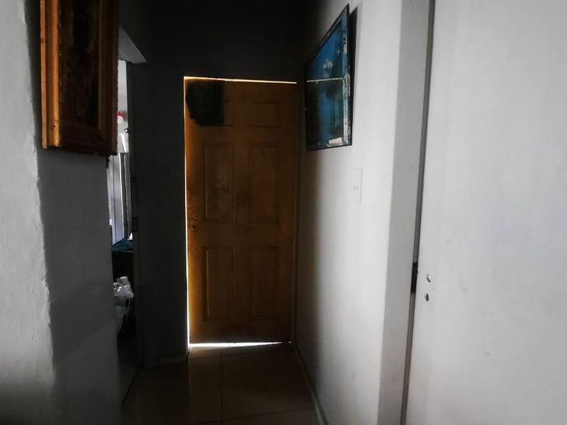 A narrow interior hallway featuring tiled flooring and a timber door, requiring cosmetic updates to improve the overall aesthetic.