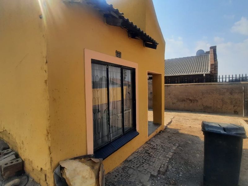 Rear exterior view of the property showing yellow painted walls, security bars on windows, and a surrounding brick boundary wall.
