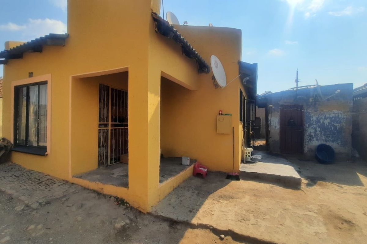 Rear view of a yellow-painted house featuring a small covered patio area and a concrete yard space.