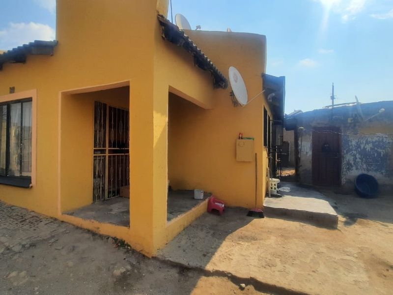 Rear view of a yellow-painted house featuring a small covered patio area and a concrete yard space.