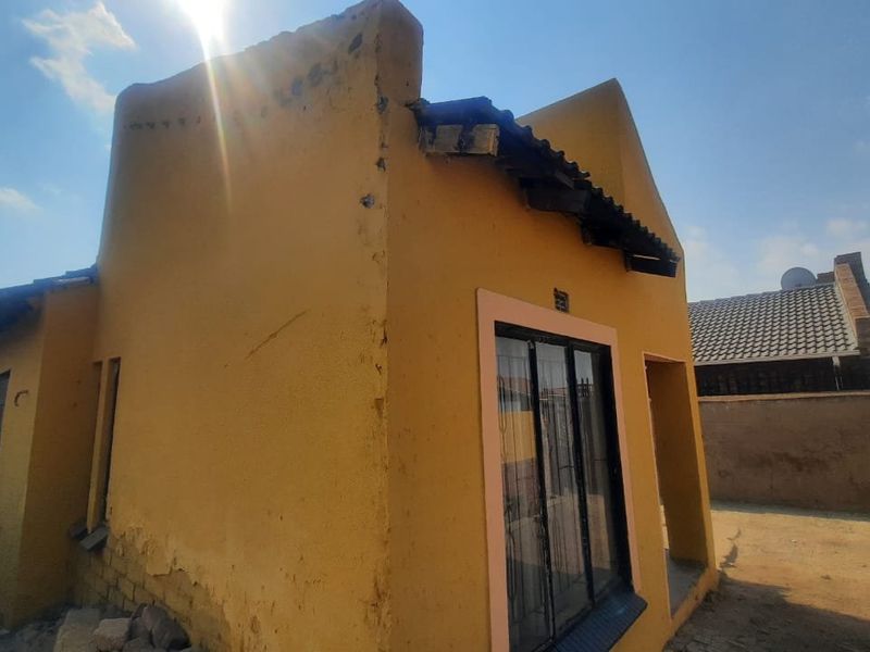 Front exterior view of a house showing plastered walls, a sliding glass door, and visible signs of structural wear and maintenance requirements.