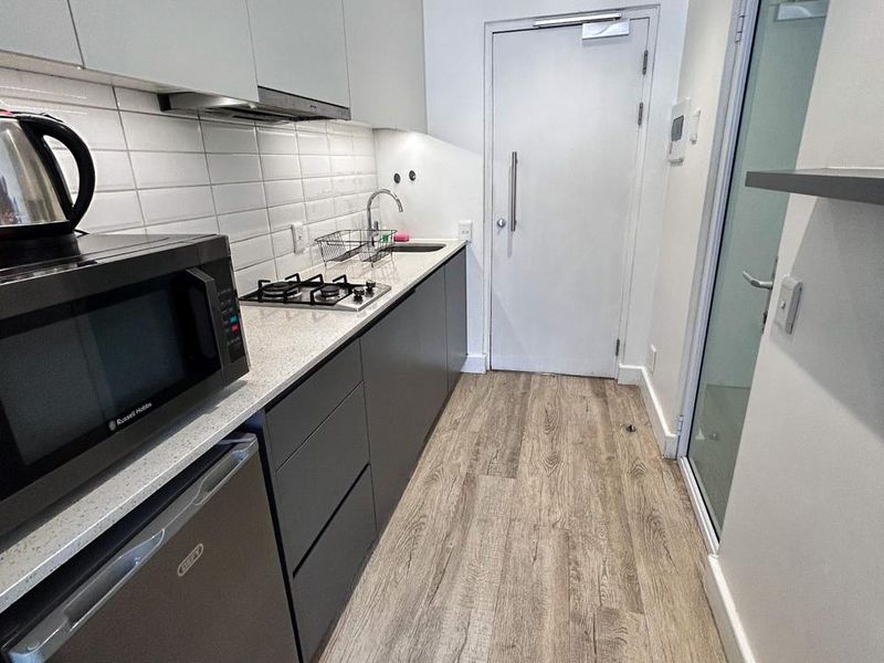 A modern, compact galley-style kitchen featuring sleek cabinetry, a gas hob, integrated extractor fan, and durable laminate flooring.