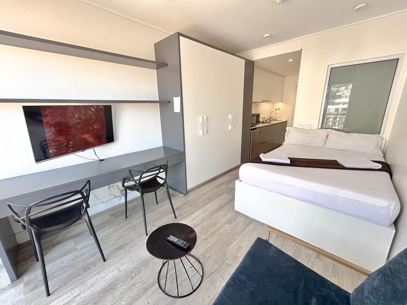 Modern open-plan studio apartment featuring a built-in desk, ample wardrobe storage, and a compact kitchenette with contemporary finishes.