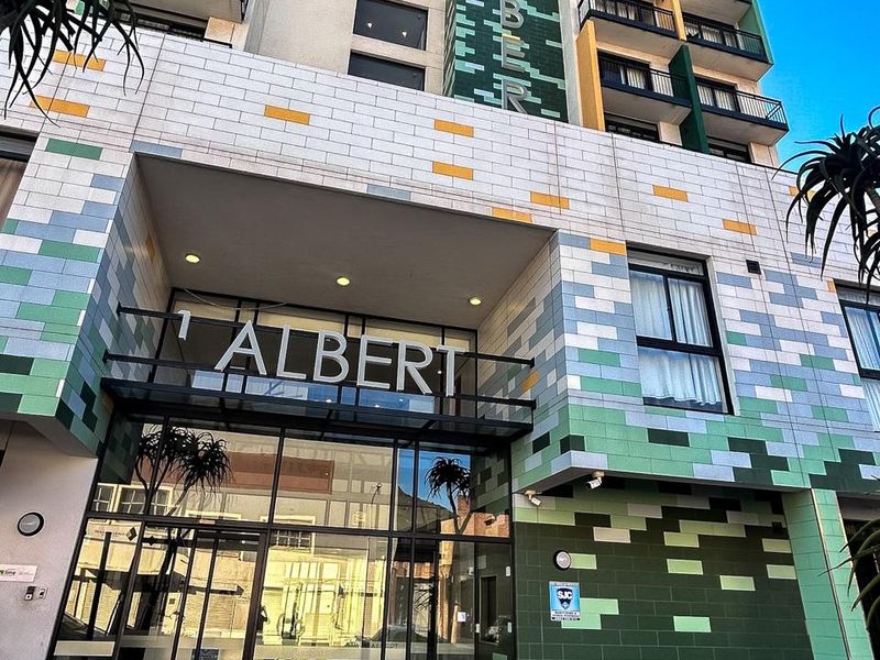 Modern apartment building facade featuring a decorative tiled exterior, glass entrance lobby, and multiple balconies.