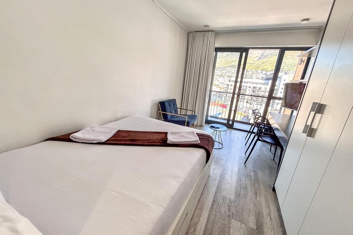 A bright bedroom featuring laminate flooring, a built-in wardrobe, and a sliding glass door leading to a balcony with city and mountain views.