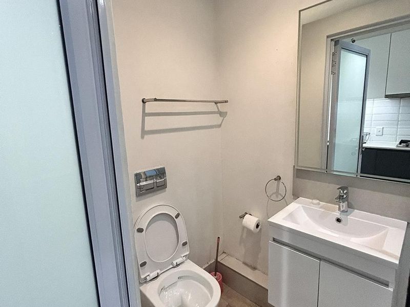 A modern, compact bathroom featuring a wall-mounted toilet, a sleek vanity with a washbasin, and a large wall mirror.