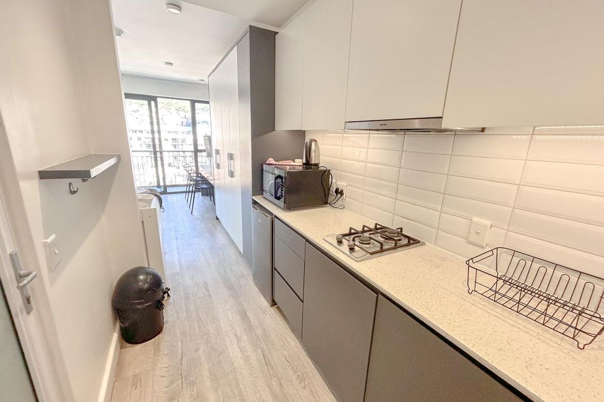 Modern galley-style kitchen featuring sleek handleless cabinetry, stone countertops, a gas hob with extractor fan, and a clean subway tile backsplash.