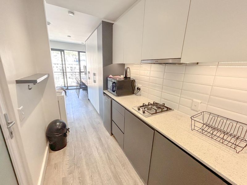 Modern galley-style kitchen featuring sleek handleless cabinetry, stone countertops, a gas hob with extractor fan, and a clean subway tile backsplash.