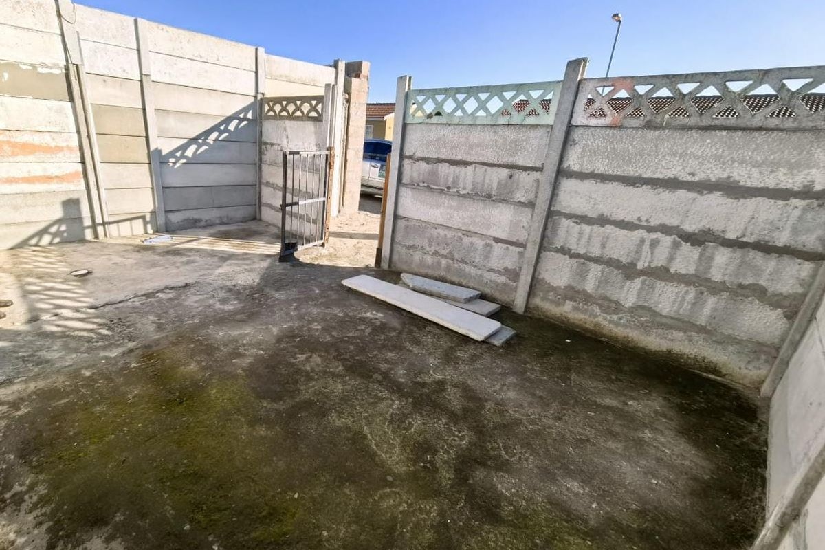 A rear outdoor area featuring precast concrete boundary walls, a metal pedestrian gate, and concrete paving requiring maintenance and cleaning.