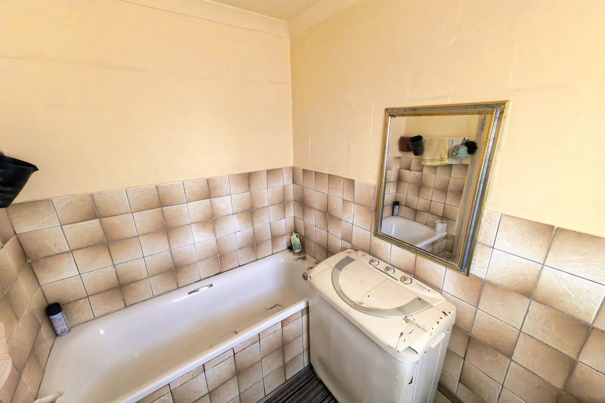A dated bathroom featuring a standard bathtub and wall tiling, requiring cosmetic updates to improve the overall aesthetic and condition.