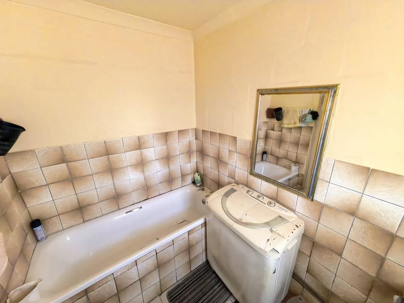 A dated bathroom featuring a standard bathtub and wall tiling, requiring cosmetic updates to improve the overall aesthetic and condition.