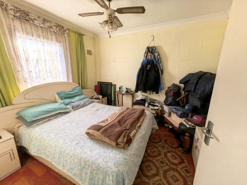 A bedroom featuring a ceiling fan and exposed blockwork walls, offering a functional space with potential for cosmetic updates.
