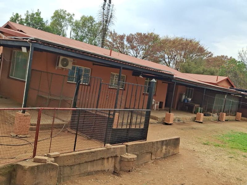 Rear view of the farm dwelling featuring a covered patio area, metal roofing, and perimeter fencing with a retaining wall.
