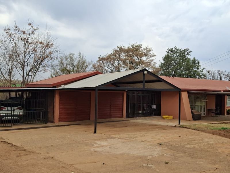 Front view of a farm property featuring a large concrete driveway, attached carport, and garage access with security gates.