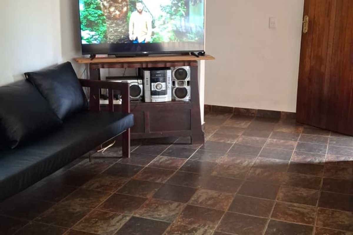 A living room area featuring dark slate-style floor tiles and a solid wooden door, providing a functional and neutral space.