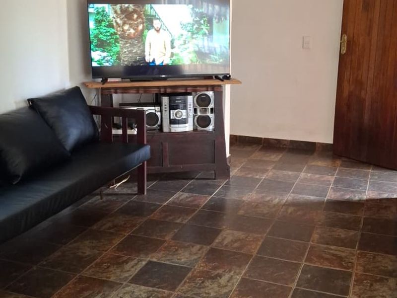 A living room area featuring dark slate-style floor tiles and a solid wooden door, providing a functional and neutral space.