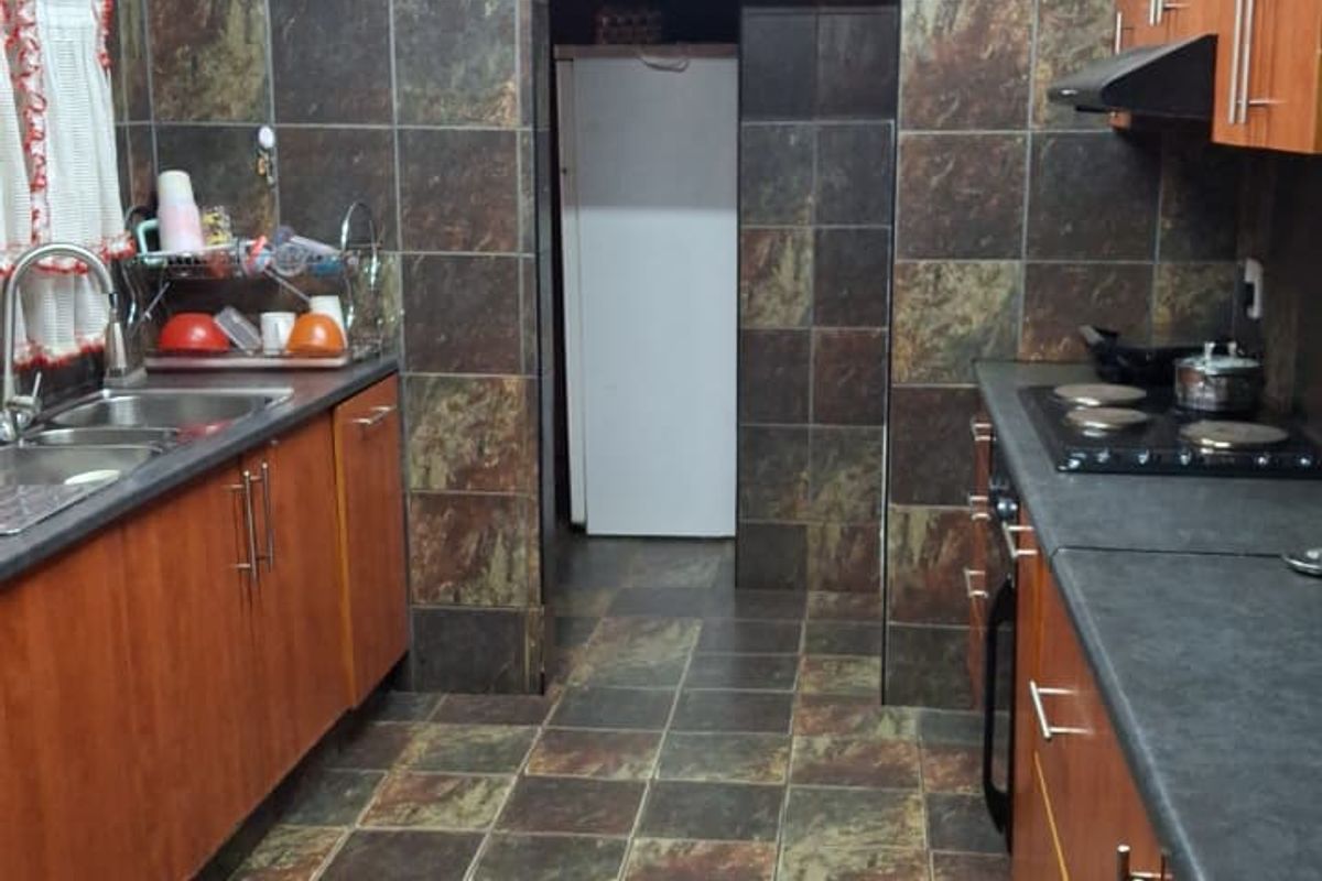 A functional kitchen featuring wood-finish cabinetry, dark laminate countertops, integrated hob with extractor, and full-height tiled wall finishes.
